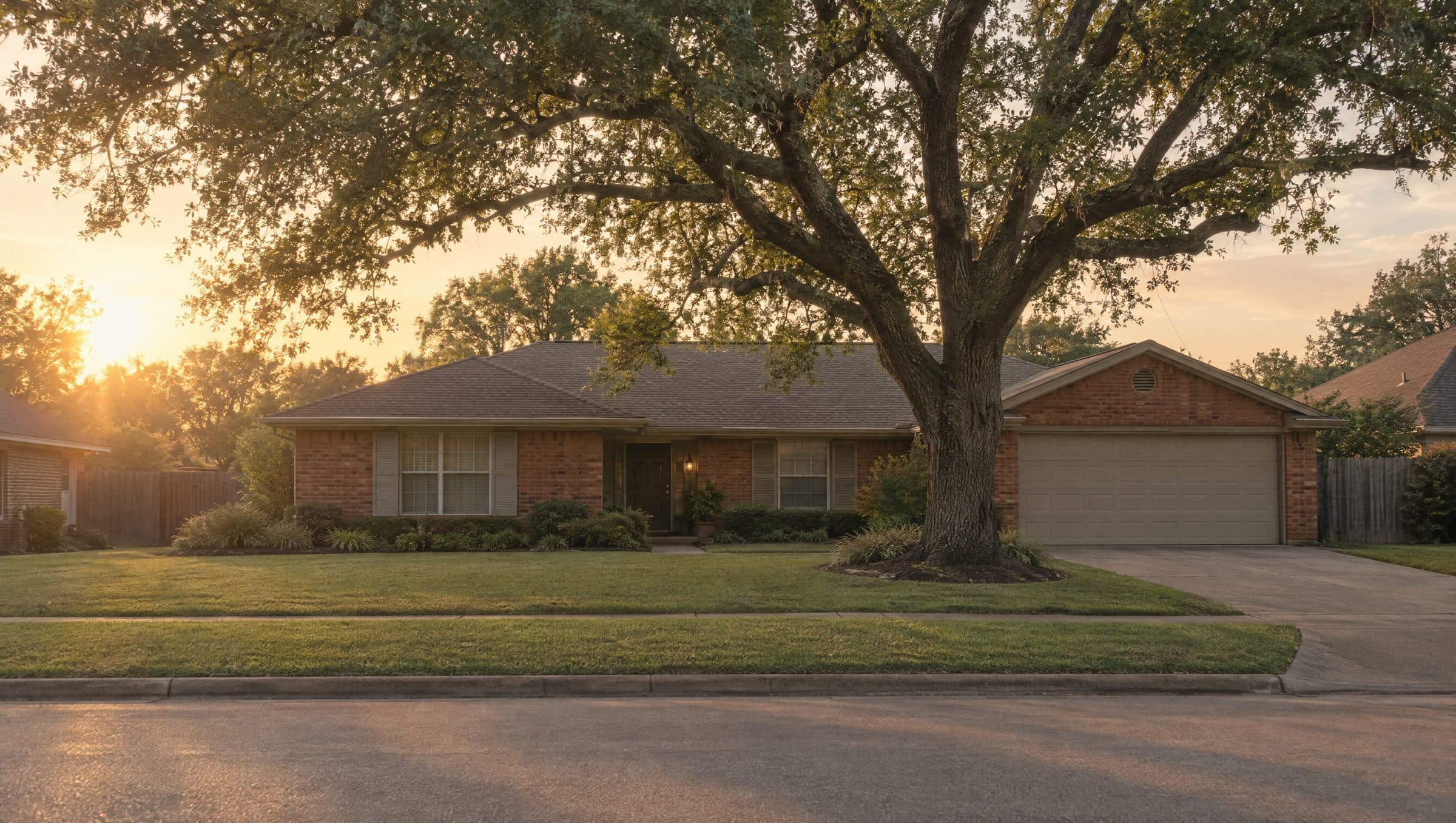 A one-story brick ranch house under a live oak at sunset.